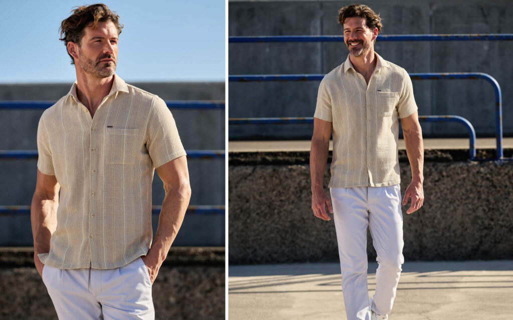 Ein Model trägt ein beiges Kurzarmhemd und eine helle Hose der Marke emilio adani vor einer sonnigen, urbanen Kulisse mit Geländer.