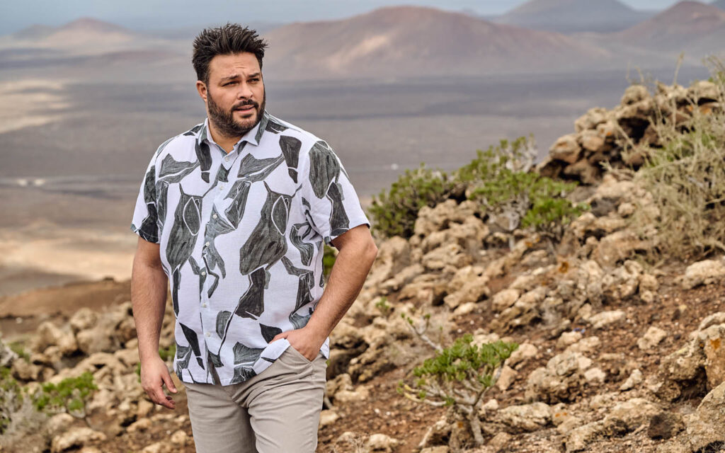 Sommerliches Outfit in naturnaher Umgebung Mann trägt kurzärmeliges, gemustertes engbers Hemd und helle Hose in felsiger Landschaft.