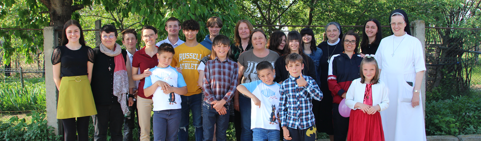 Gruppenbild Gruppe von Kindern und erwachsenen Personen steht gemeinsam im Freien vor Bäumen und einem Zaun.