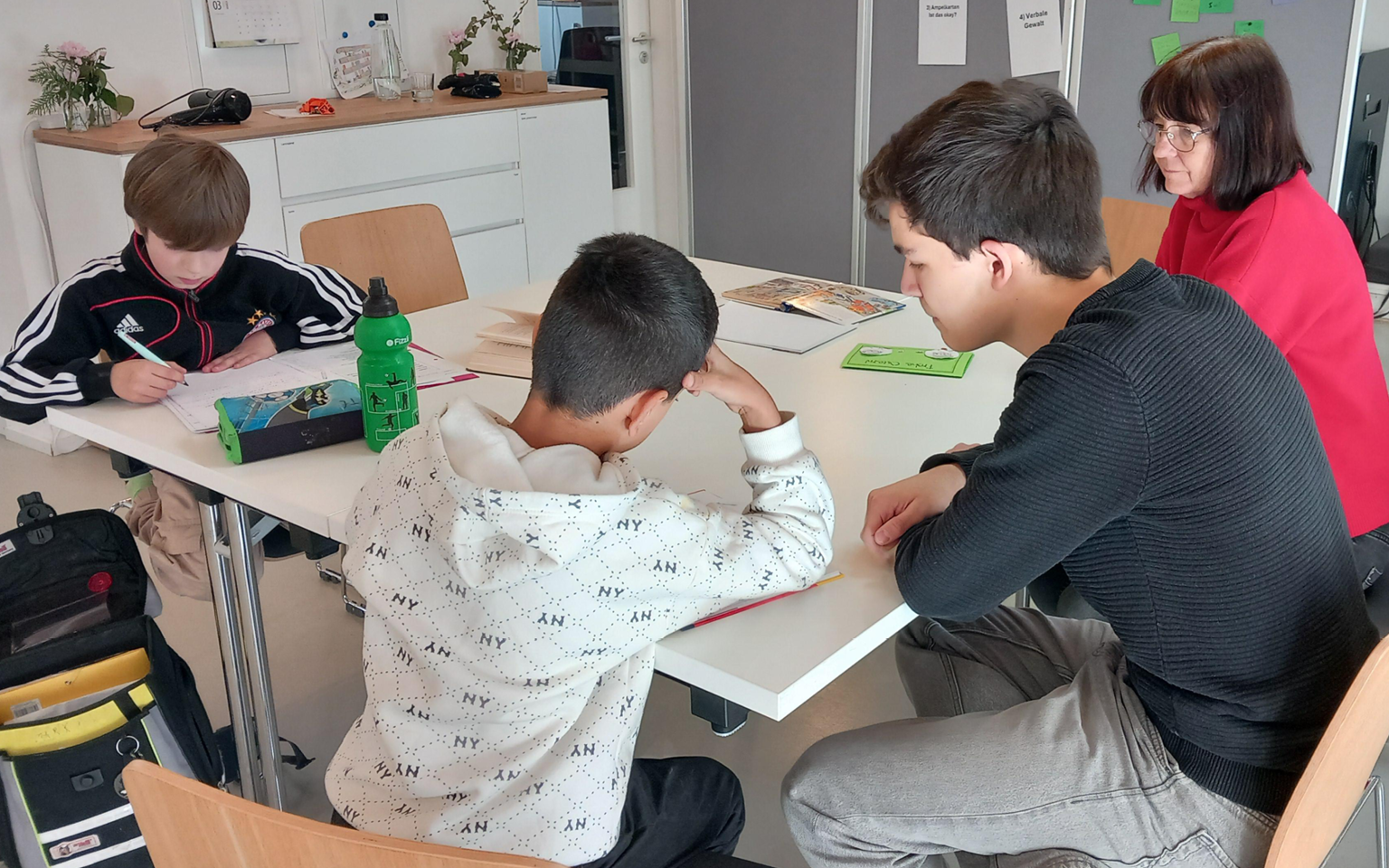 Gemeinsames Lernen im Förderprojekt der Bernhard-Bosch-Stiftung Innenaufnahme eines Lernraums mit mehreren Kindern und einer erwachsenen Person, die gemeinsam an einem Tisch sitzen.