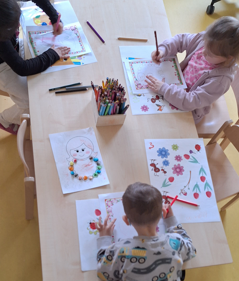 Mehrere Kinder sitzen an einem Tisch und gestalten Bilder mit Stiften, Farben und Bastelmaterialien.