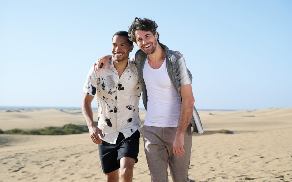 Zwei Personen in luftigen emilio adani Sommer-Outfits in einer Dünenlandschaft.