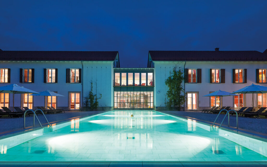 Außenpool Rechts zeigt ein beleuchteter Außenpool vor einer Hotelanlage in den Abendstunden.