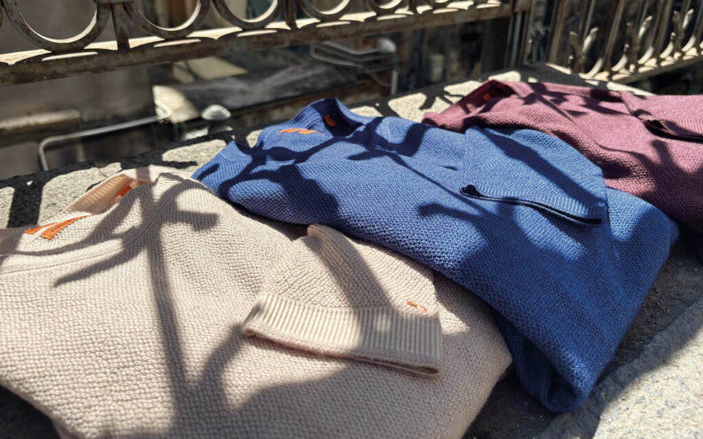 Gefaltete Strickpullover in Beige, Blau und Bordeaux Drei hochwertige Strickpullover in Beige, Blau und Bordeaux präsentieren sich stilvoll im natürlichen Licht und zeigen die Vielseitigkeit moderner Herbstmode.